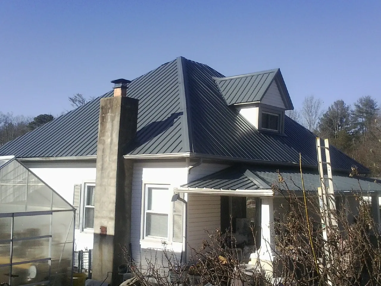 Dark blue standing seam metal roof on a white farmhouse with dormer — Slate & Tile Roof Repair by Roofing Brothers in Springfield